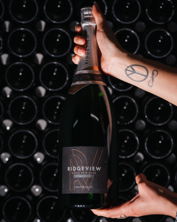 Ridgeview Wine Estate, English Sparkling Wine, Blanc de Blancs held up in front of bottles in our cellar