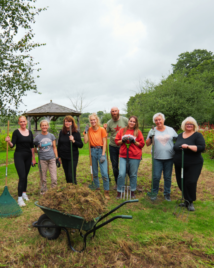 8 team members standing with rakes and a wheel barrow, volunteer gardening at Chessnut Tree House Children's Hospice