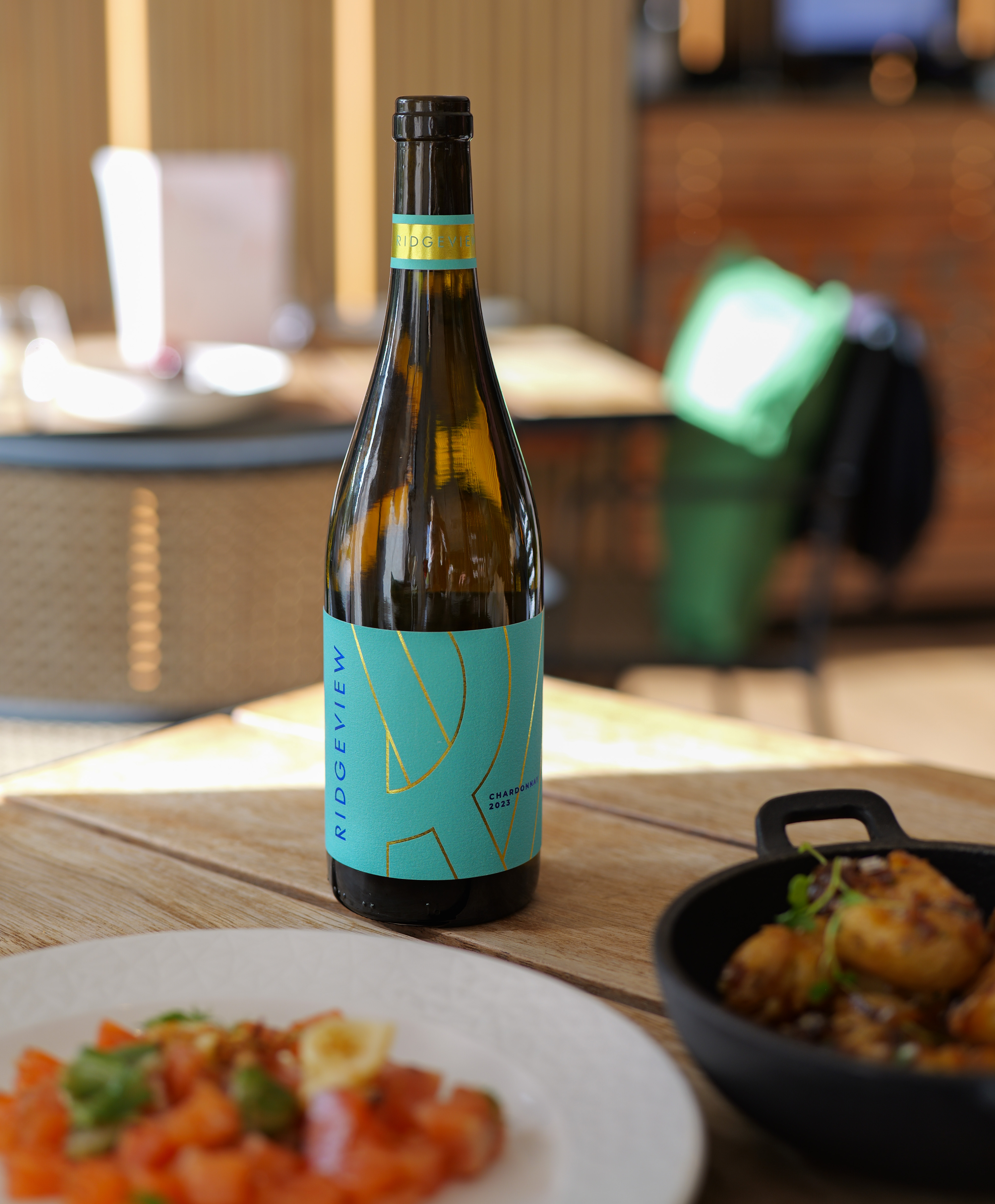 A bottle with a green label on a table in a restaurant with food around it