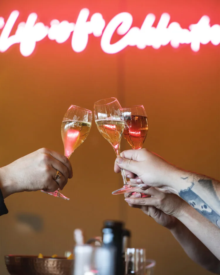 clinking wine classes with light sign behind